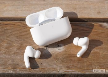 The AirPods Pro 2 sitting outside their case on a wooden surface with the case nearby.