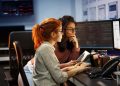 Two developers collaborate on a project as they review code on a display in their workspace.